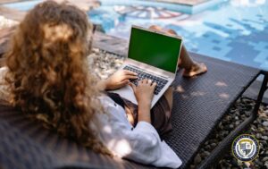 Kobieta, grafik z kręconymi włosami pracująca zdalnie na laptopie przy basenie