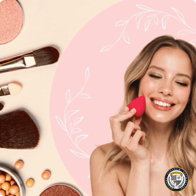 Uśmiechnięta młoda kobieta z naturalnym makijażem aplikuje podkład czerwoną gąbeczką beauty blender, obok widoczne pędzle do makijażu i kosmetyki w ciepłych odcieniach na beżowo-różowym tle z dekoracyjnymi białymi listkami