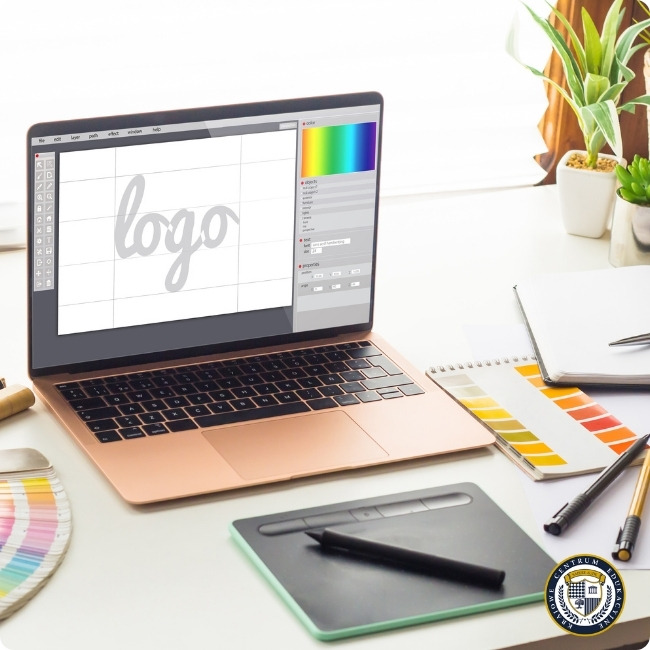 Stanowisko pracy grafika z różowym laptopem wyświetlającym program do projektowania logo, tabletem graficznym, próbnikami kolorów i roślinami dekoracyjnymi w tle
