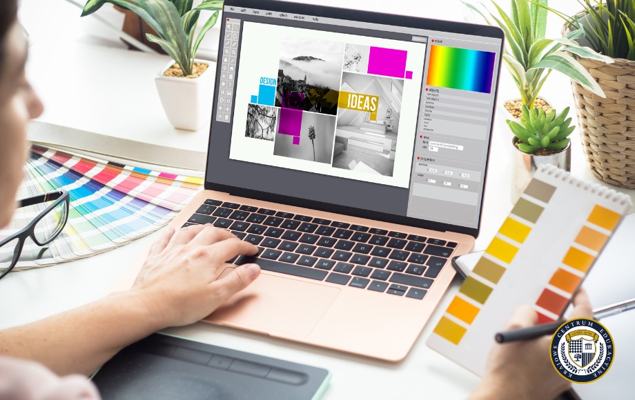 Projektant pracujący w darmowym programie graficznym na laptopie, obok znajdują się próbniki kolorów, tablet graficzny oraz rośliny doniczkowe na jasnym biurku