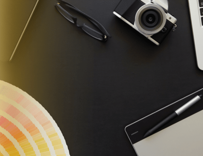 Minimalistyczne biurko z aparatem fotograficznym, długopisem i próbnikiem kolorów Pantone na czarnym tle