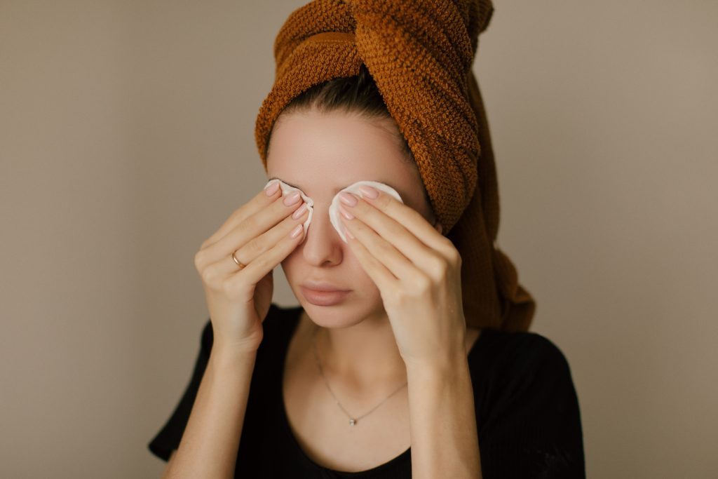 Kobieta w turbanie z ręcznika zmywa makijaż przy użyciu płatków kosmetycznych