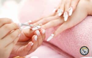 Profesjonalne zdobienia paznokci – stylistka paznokci precyzyjnie ozdabia dłonie klientki, dodając eleganckie detale do białego manicure z kryształkami
