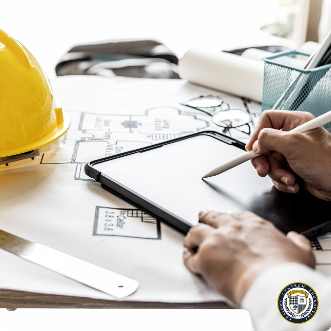 Skala w AutoCAD - Specjalista budowlany korzystający z tabletu przy przeglądaniu planów architektonicznych. Widoczny żółty kask, narzędzia kreślarskie i zwinięte plany