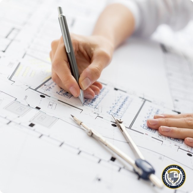 Zbliżenie na rękę architekta rysującą linie w AutoCAD z użyciem metalowego pióra na wydrukowanym planie budynku. Obok widać narzędzia kreślarskie używane do precyzyjnego projektowania