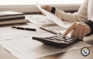 Samodzielny księgowy wykonujący obliczenia na kalkulatorze przy biurku z dokumentami księgowymi, obrazujący codzienną pracę z dokumentacją finansową