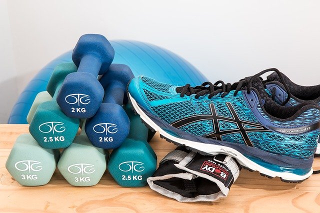 Ciężarki do ćwiczeń oraz buty sportowe leżące na stole. W tle piłka do pilatesu.