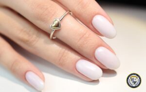 Delikatny manicure klasyczny - eleganckie paznokcie w mleczno-białym kolorze z subtelnym połyskiem, idealnie podkreślające srebrny pierścionek z motywem serca.