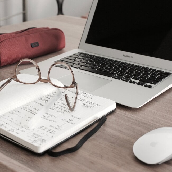 Okulary, notatnik i otwarty laptop na biurku