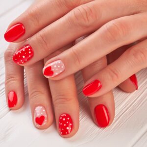 Female hands with polished nails. Woman gentle hands with red hearts and dots design manicure on white wooden background close up.