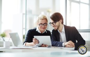 Dwoje profesjonalistów przeglądających materiały szkoleniowe na tablecie - kobieta i mężczyzna w okularach uśmiechają się podczas planowania szkoleń i kursów online dla pracowników w nowoczesnym biurze