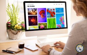 Kobieta siedzi przy biurku w jasnym wnętrzu i przegląda na dużym monitorze komputerowym kolorowe fotografie przyrodnicze w swoim portfolio, otoczone elementami dekoracyjnymi i kubkiem kawy.
