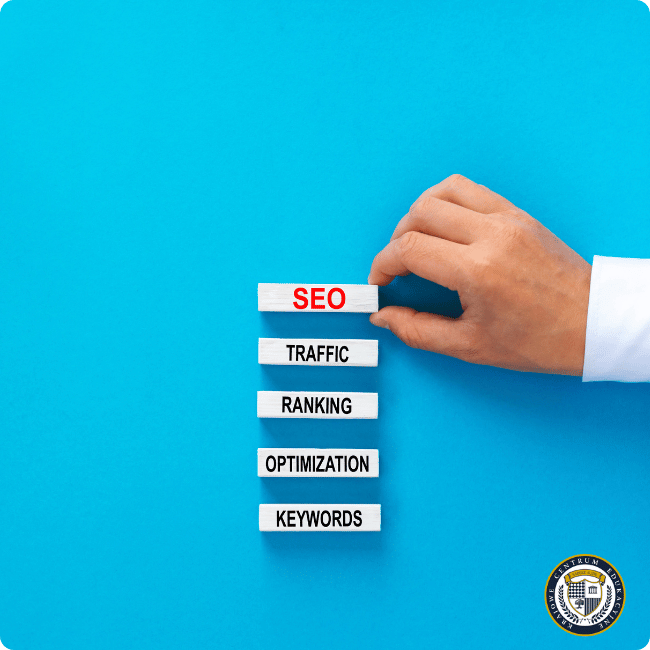 Ręka w białym rękawie układająca pionowo białe klocki z czarnymi napisami związanymi z SEO: od góry SEO (w kolorze czerwonym), TRAFFIC, RANKING, OPTIMIZATION i KEYWORDS na turkusowym tle. W prawym dolnym rogu znajduje się okrągłe logo KCE