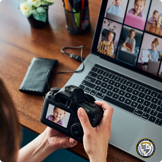 Osoba przy biurku trzyma cyfrową lustrzankę z wyświetlonym zdjęciem dziecka, a obok na ekranie laptopa widnieją miniatury innych fotografii