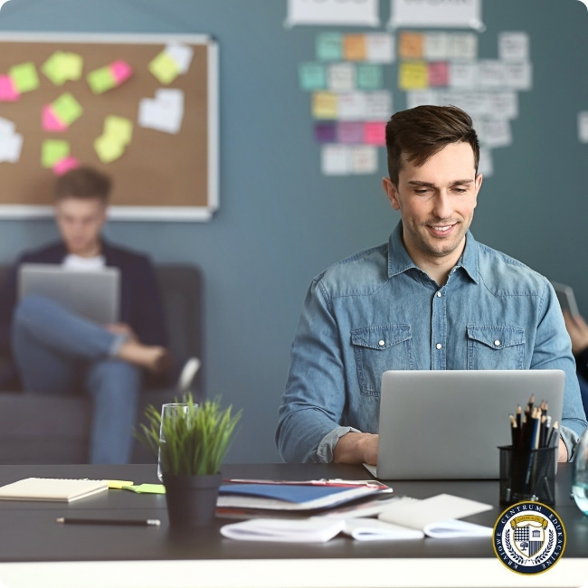 Specjalista ds. marketingu zarobki: Młody specjalista ds. marketingu pracujący przy laptopie w nowoczesnym biurze. W tle tablica z kolorowymi karteczkami i notatkami, przedstawiająca mapę projektów marketingowych