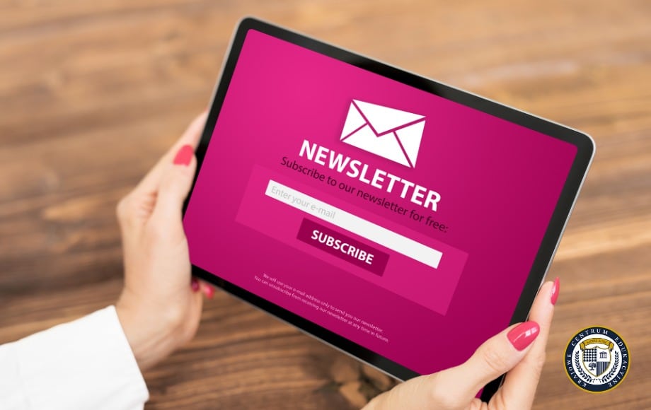 Formularz zapisu do newslettera na różowym ekranie tabletu - przykład zastosowania e-mail marketingu w praktyce. Widoczne białe pole do wpisania adresu e-mail oraz przycisk 'Subscribe', trzymany w dłoniach z różowym manicure.
