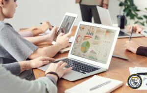 Zespół specjalistów analizuje wyniki kampanii Google Ads na laptopie wyświetlającym kolorowe wykresy i statystyki efektywności reklam. Na drewnianym stole widoczne są również urządzenia mobilne używane do monitorowania kampanii w czasie rzeczywistym