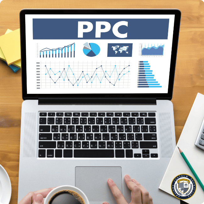 Laptop na drewnianym biurku wyświetlający dashboard z napisem "PPC" i różnorodne wykresy analityczne, wizualizacje danych oraz mapę świata, obok widoczna filiżanka kawy.