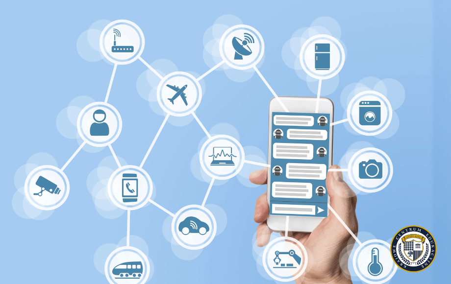 Grafika pokazująca czym jest chatbot - dłoń trzymająca smartfon z interfejsem czatu, połączony siecią z różnymi ikonami urządzeń IoT (router, antena, lodówka, pralka, aparat, osoba, kamera, telefon, pojazdy, monitor). Wizualizacja przedstawia chatbota jako centralny punkt komunikacji w inteligentnym ekosystemie urządzeń