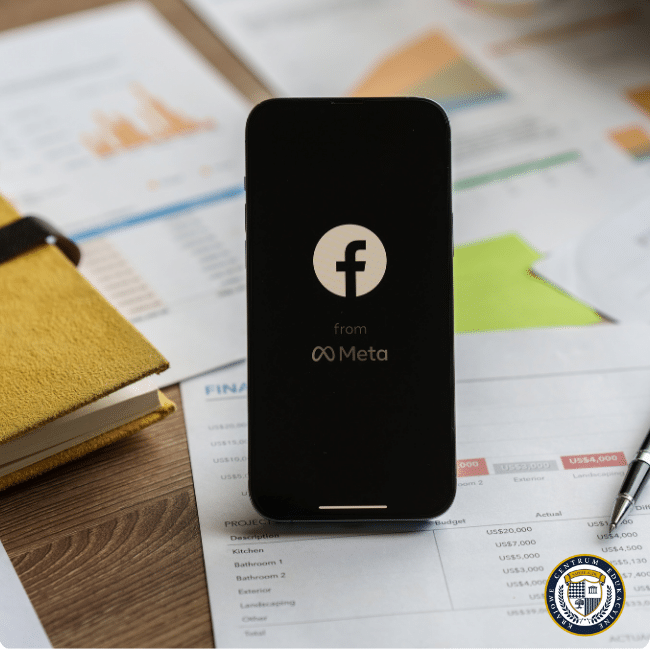 Smartfon z logo Facebooka i napisem 'from Meta' na ekranie, leżący na dokumentach z wykresami i danymi analitycznymi dotyczącymi reklamy na Facebooku