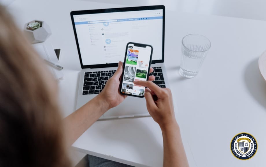 Osoba przeglądająca reklamy na Facebooku na smartfonie, siedząca przy biurku z laptopem, szklanką wody i małą rośliną. Reklama na Facebooku widoczna na ekranie telefonu pokazuje różne obrazy produktów