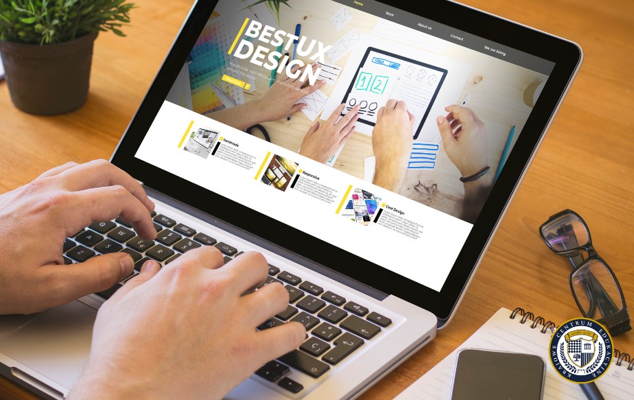 Osoba pracująca na laptopie z widoczną stroną internetową dotyczącą projektowania, pokazująca praktyczne tworzenie strony WordPress w profesjonalnym środowisku pracy z notatnikiem i okularami obok