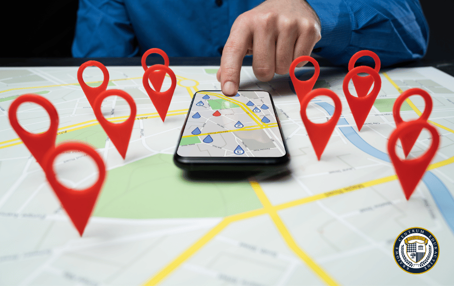 Ręka wskazująca na smartfon z mapą otoczoną czerwonymi pinezkami lokalizacji, reprezentujące lokalne SEO.