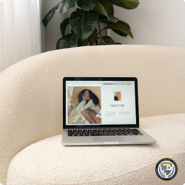 Laptop na kremowej sofie wyświetlający portfolio lub stronę 'About Me' z fotografią kobiety, część strategii komunikacji marki osobistej w minimalistycznym, domowym otoczeniu z rośliną w tle