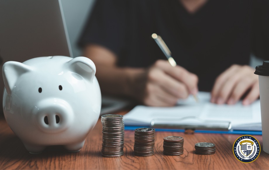 Osoba wypełniająca dokumenty przy biurku ze skarbonką i monetami - ilustracja procesu ubiegania się o dofinansowanie do szkolenia