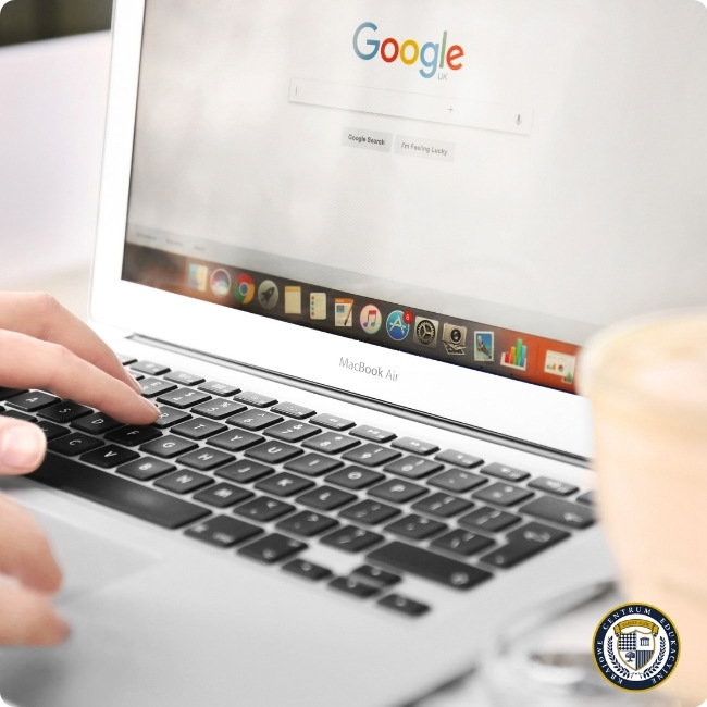Osoba używająca laptopa MacBook Air z otwartą stroną wyszukiwarki Google, widok z góry na klawiaturę i ekran