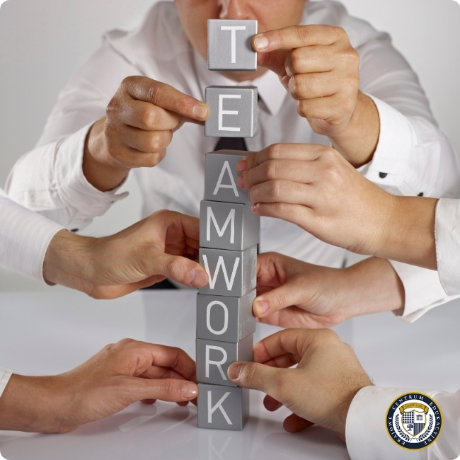Ręce różnych osób układające szare klocki z literami tworzącymi słowo TEAMWORK