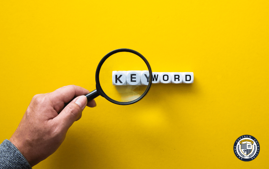 Dłoń trzymająca lupę nad kostkami tworzącymi słowo "KEYWORD" na żółtym tle - skuteczne słowa kluczowe w Google Ads to podstawa efektywnych kampanii reklamowych.