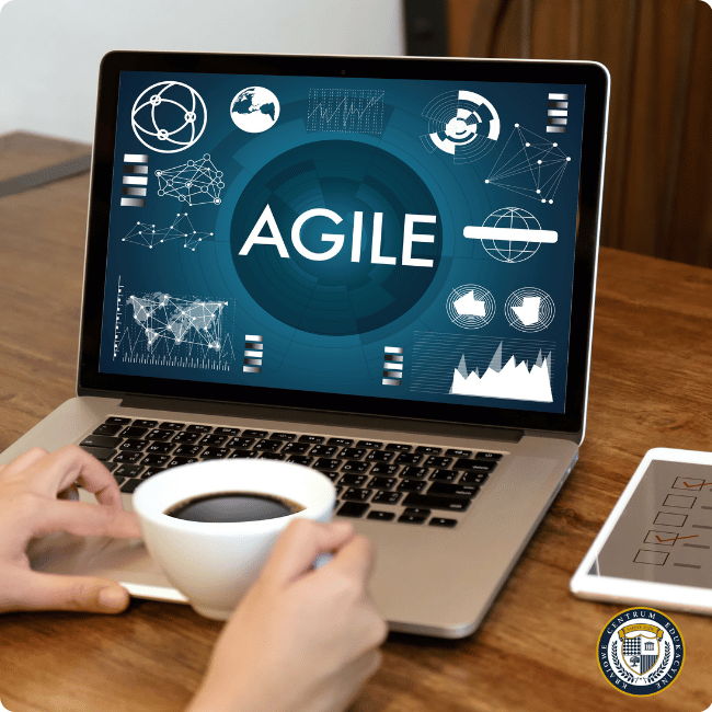 Laptop wyświetlający prezentację o metodyce Agile z wykresami i ikonami, osoba trzymająca filiżankę kawy przy biurku.