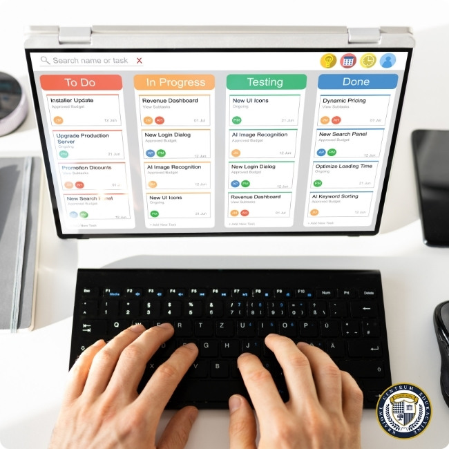 Monitor komputera wyświetlający tablicę Kanban z czterema kolumnami zadań: To Do, In Progress, Testing i Done, ręce na klawiaturze.