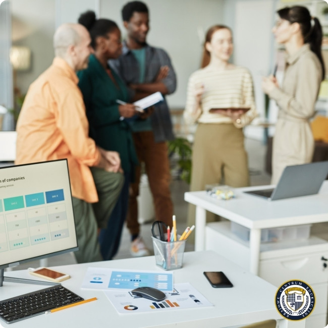 Zespół pracowników podczas spotkania Agile w biurze, na pierwszym planie monitor z wykresami, w tle grupa osób dyskutująca przy tablicy.