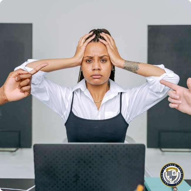 Kobieta przy laptopie trzyma się za głowę z wyrazem frustracji, podczas gdy dwie ręce wyciągają się w jej kierunku - ilustracja przeciążenia krytyką w pracy