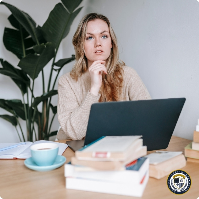 Kobieta zastanawia się nad projektem przy laptopie, otoczona książkami, ilustrując proces myślenia podczas pracy z design thinking.