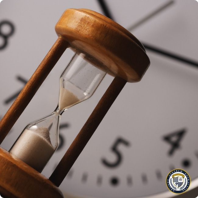 Efektywne zarządzanie czasem - drewniana klepsydra z piaskiem na tle zegara