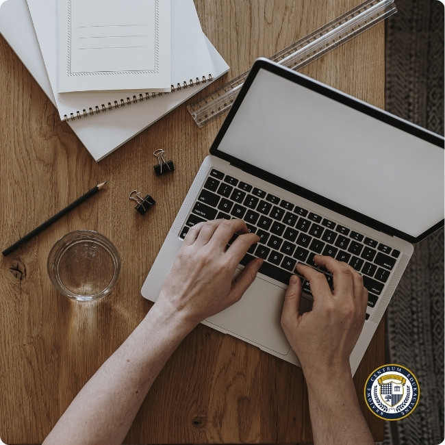 Osoba pisząca ogłoszenie o pracę na laptopie przy biurku z notatnikami i materiałami biurowymi