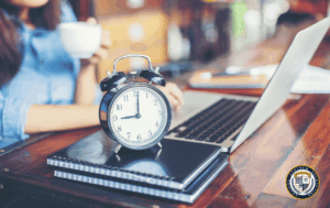 Zegar i laptop na stole przy kawie, ilustrujące techniki zarządzania czasem, takie jak technika Pomodoro