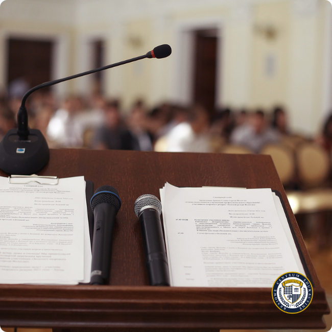 Mównica z mikrofonami i notatkami do przemówienia, w tle publiczność na konferencji