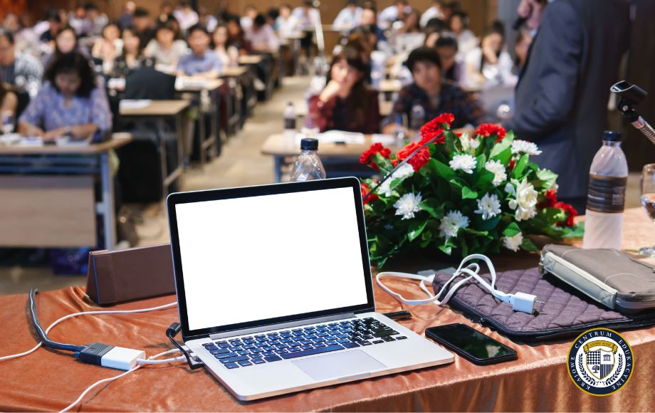 Laptop z otwartym programem do prezentacji na stole prelegenta podczas konferencji z publicznością w tle
