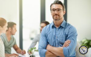 Pewny siebie mężczyzna w okularach stoi ze skrzyżowanymi rękami w biurze