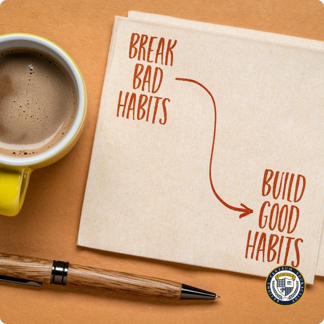 Serwetka z zapisanymi hasłami "Break Bad Habits" i "Build Good Habits" ze strzałką wskazującą kierunek zmiany, obok kubka kawy i długopisu 