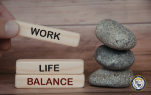 Drewniane klocki z napisami WORK, LIFE, BALANCE ułożone obok kamieni zen — grafika ilustrująca równowagę między pracą a życiem prywatnym.