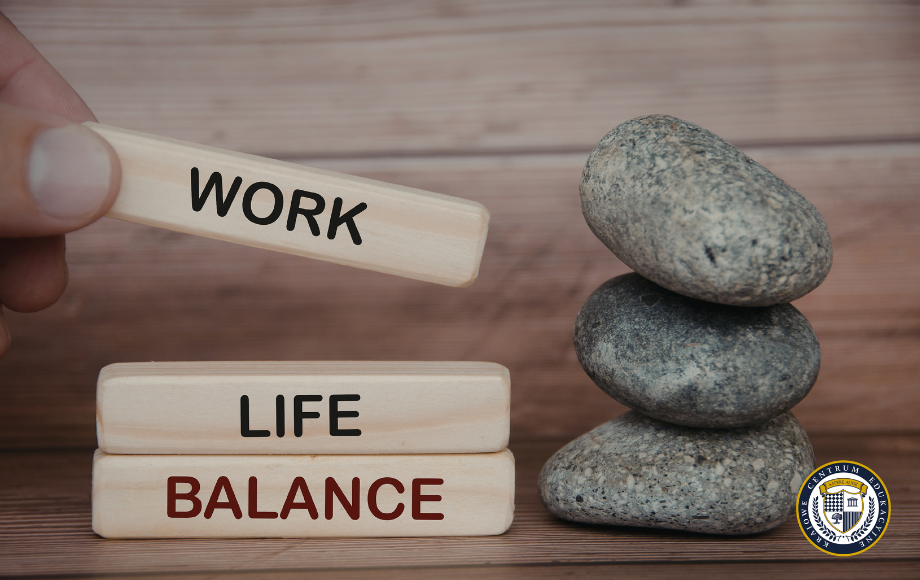 Drewniane klocki z napisami WORK, LIFE, BALANCE ułożone obok kamieni zen — grafika ilustrująca równowagę między pracą a życiem prywatnym.